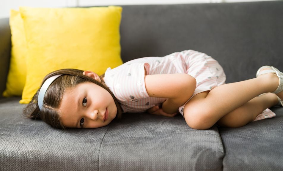 Kind liegt auf der Couch und hält sich den Bauch