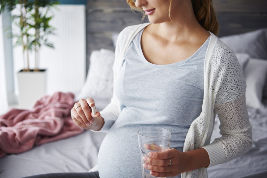 Schwangere mit einer Kapsel und einem Glas Wasser