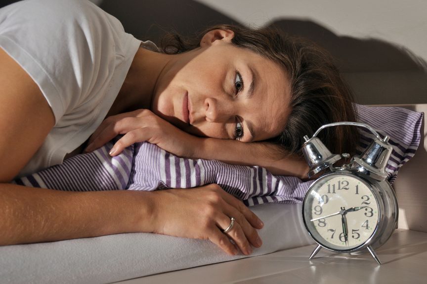 Frau liegt im Bett und schaut auf den Wecker