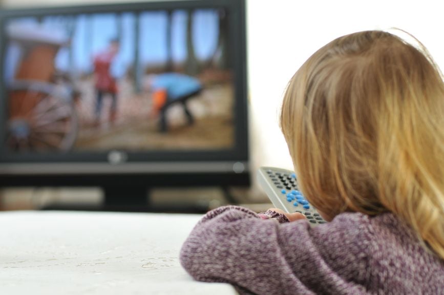 Kind vor dem Fernsehen mit Fernbedienung