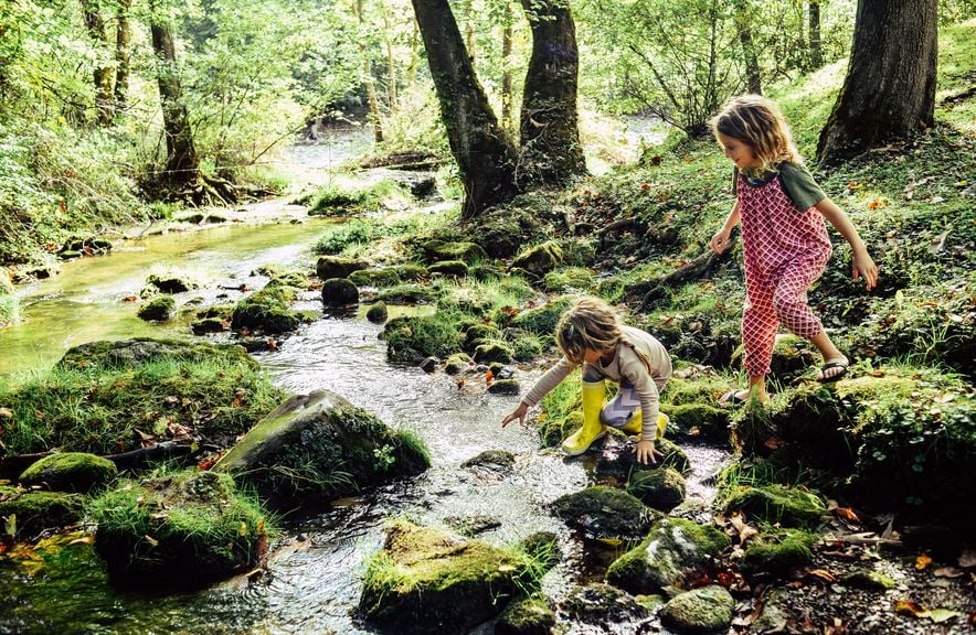 Zwei Kinder spielen an einem Bach im Wald