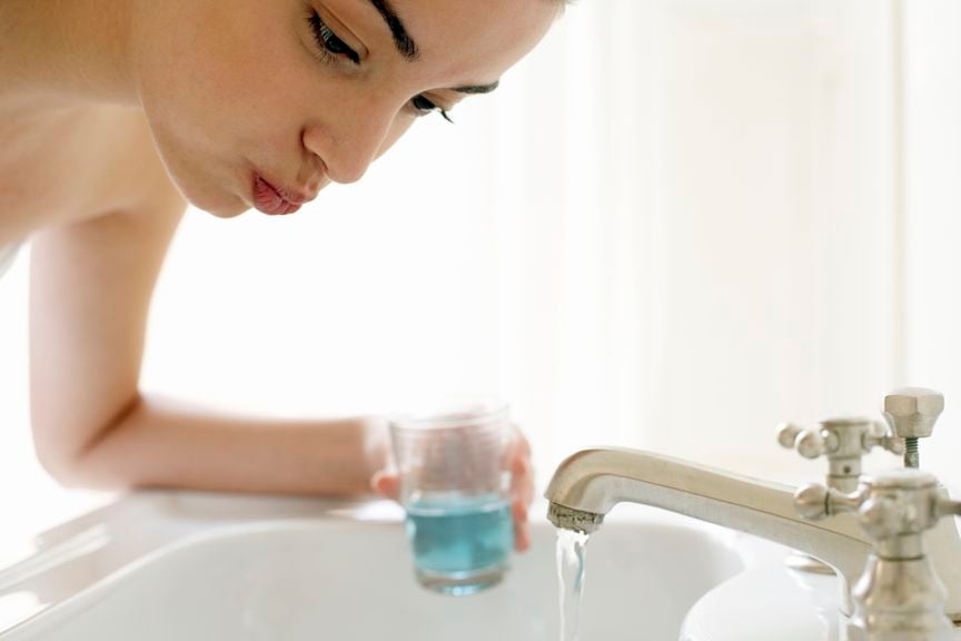 Frau am Waschbecken mit einem Glas zur Mundspülung