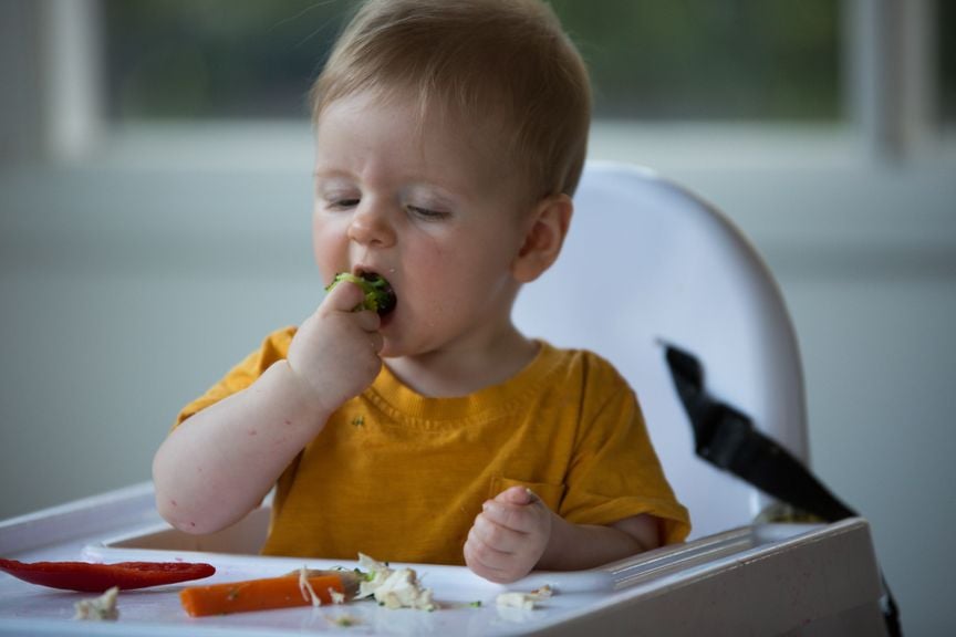 Baby sitzt im Hochstuhl und isst Fingerfood