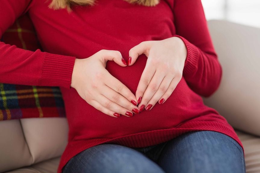 Schwangere formt ein Herz mit ihren Händen auf ihrem Bauch