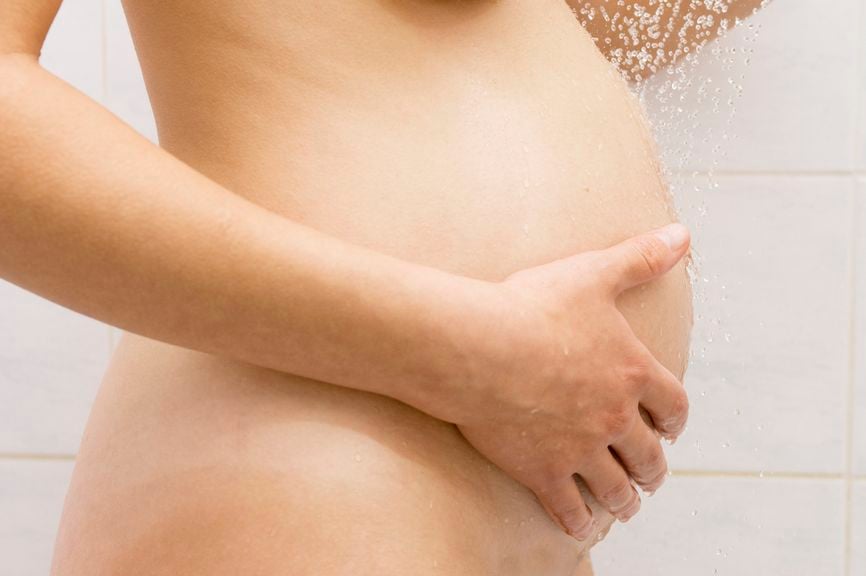 Schwangere unter der Dusche, hält sich den Babybauch