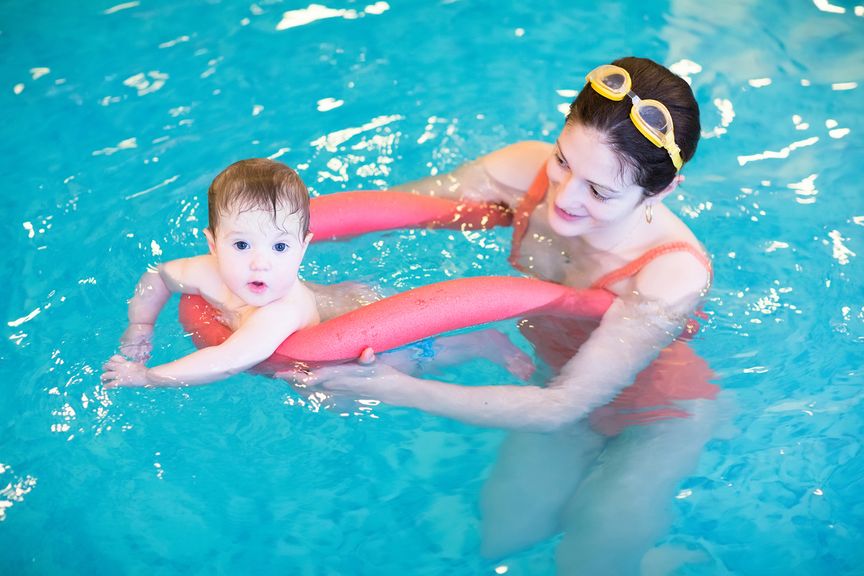 Mutter mit Baby und Poolnudel im Schwimmbad