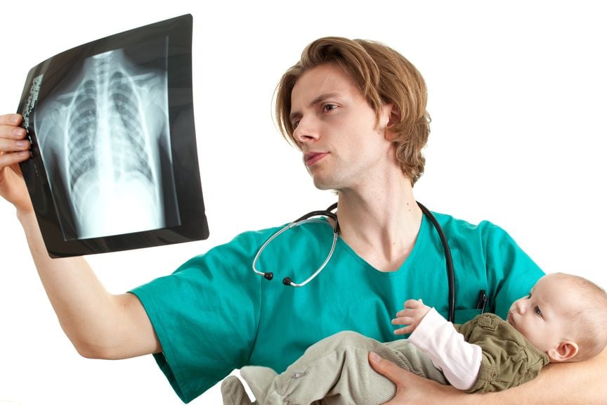 Arzt mit Baby auf dem Arm betrachtet Röntgenbild