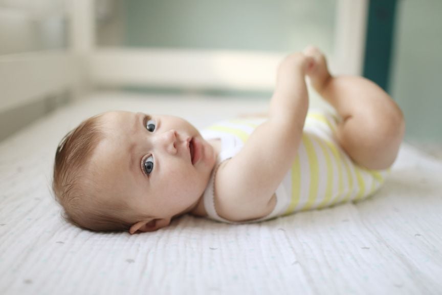 Baby liegt auf dem Rücken und fasst sich an den Fuss