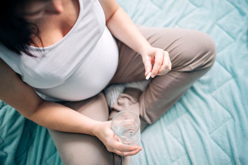 Schwangere mit Medikamenten und einem Glas Wasser