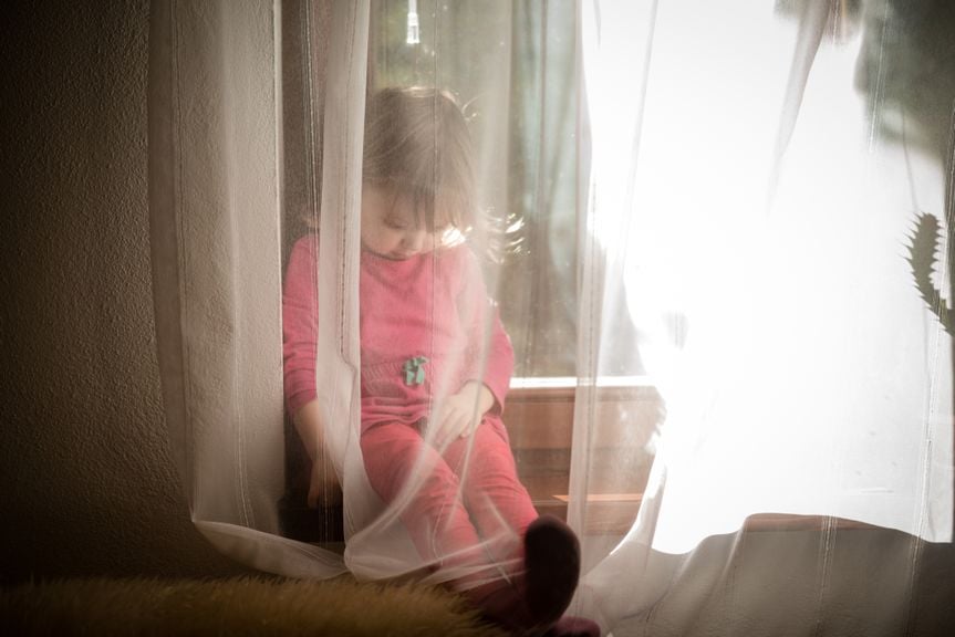 Mädchen sitzt am Fenster hinter Vorhang