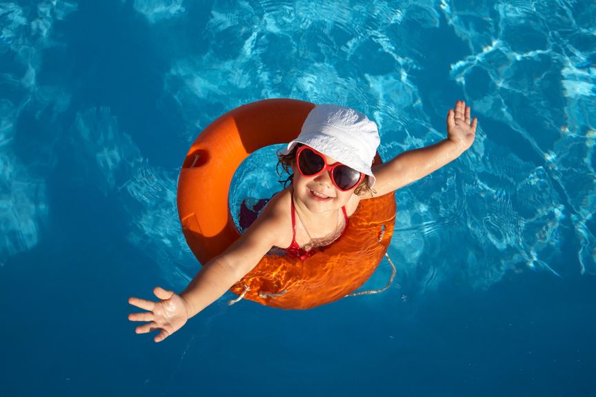 Kind mit Sonnenhut, roter Sonnenbrille und rotem Schwimmring im Pool