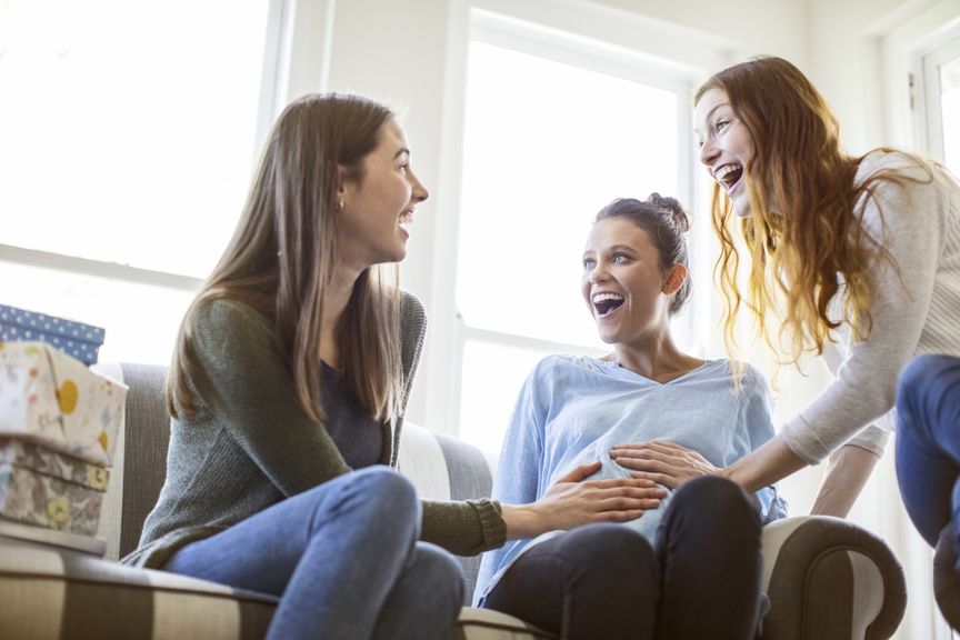 Freundinnen betasten Bauch der Schwangeren und lachen