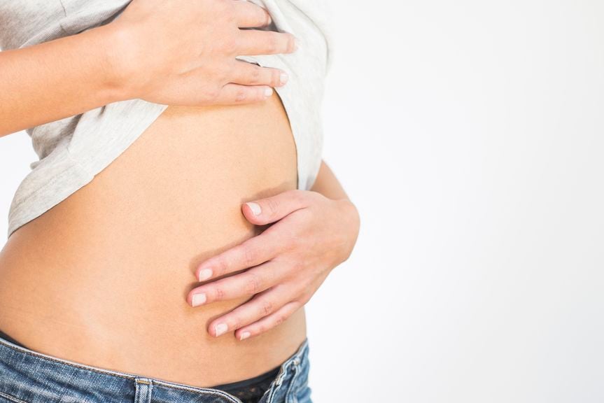 Frau hält Shirt hoch und streichelt sich über den Bauch