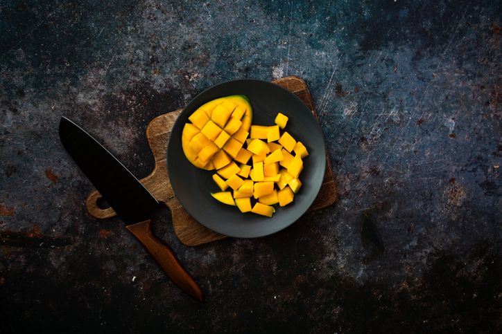 Gewürfelte Mango auf schwarzem Teller und Holz-Schneidebrett