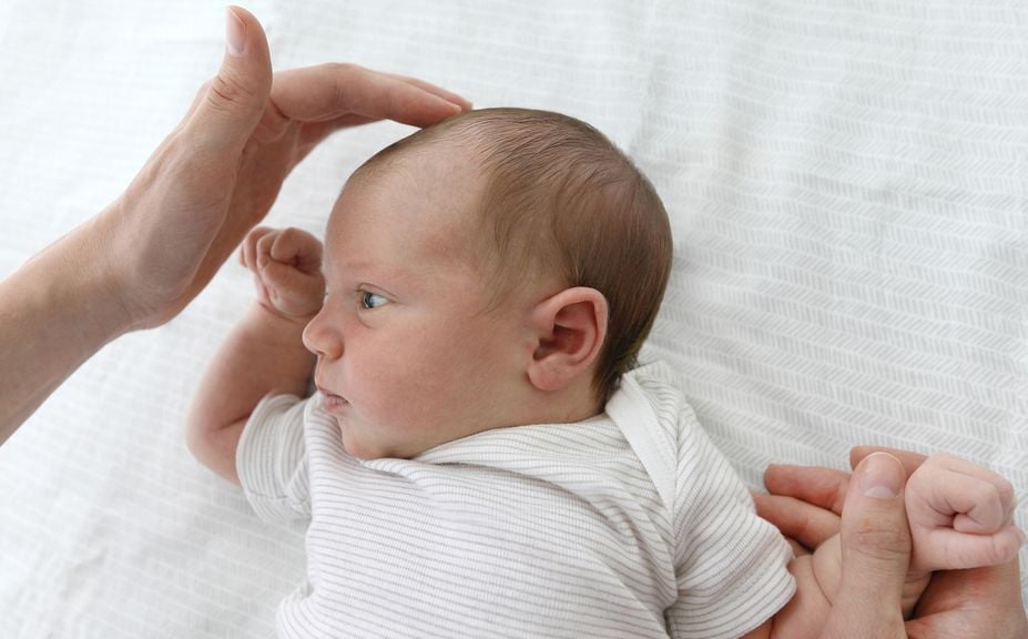 Hand fühlt beim Neugeborenen die Fontanelle