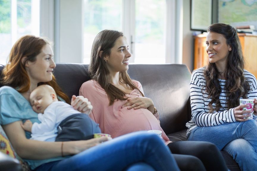 Frau mit Baby, Schwangere und Freundin auf dem Sofa