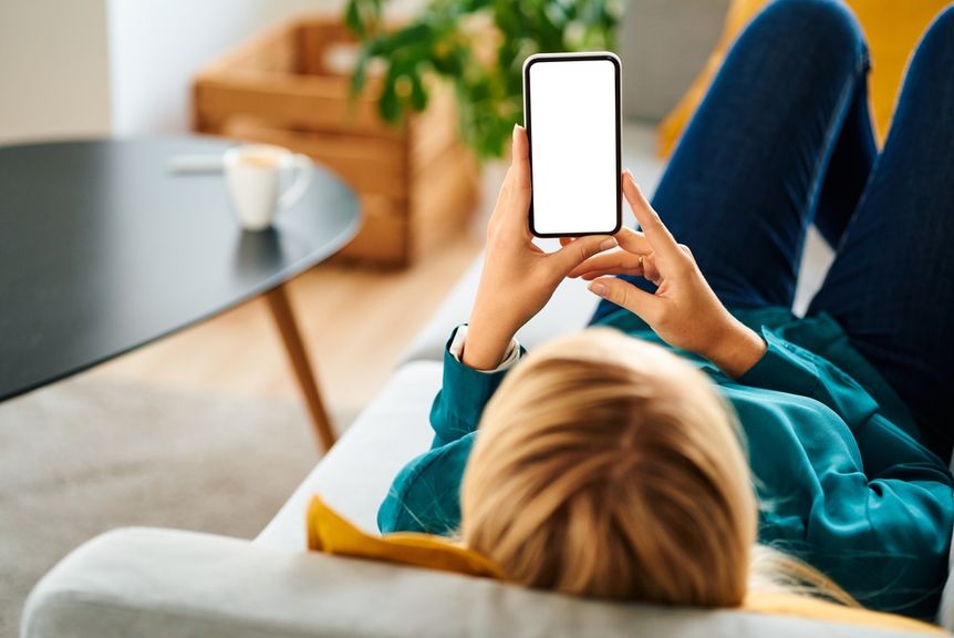 Frau liegt auf dem Sofa und schaut aufs Handy