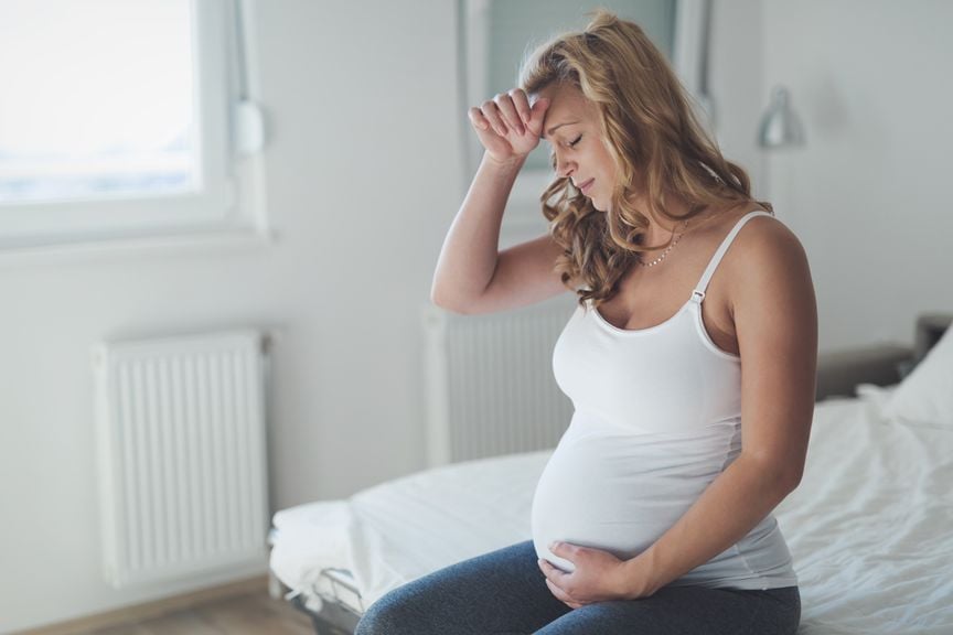 Schwangere mit Kopfschmerzen sitzt auf dem Bettrand