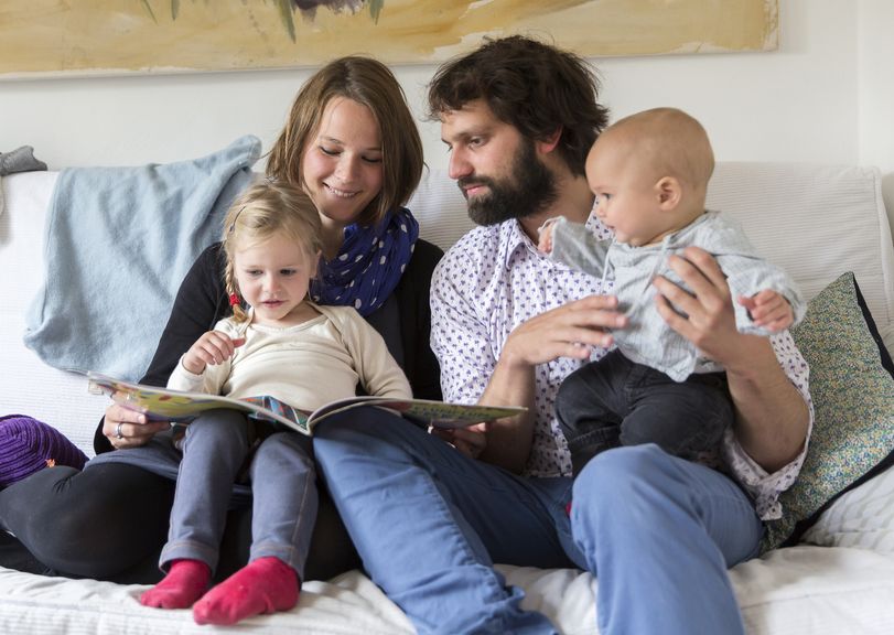 Eltern mit zwei Kindern sitzen auf dem Sofa und schauen ein Bilderbuch an