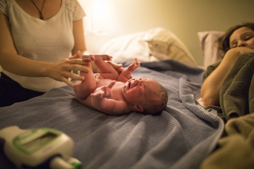 Hebamme untersucht Neugeborenes nach Hausgeburt