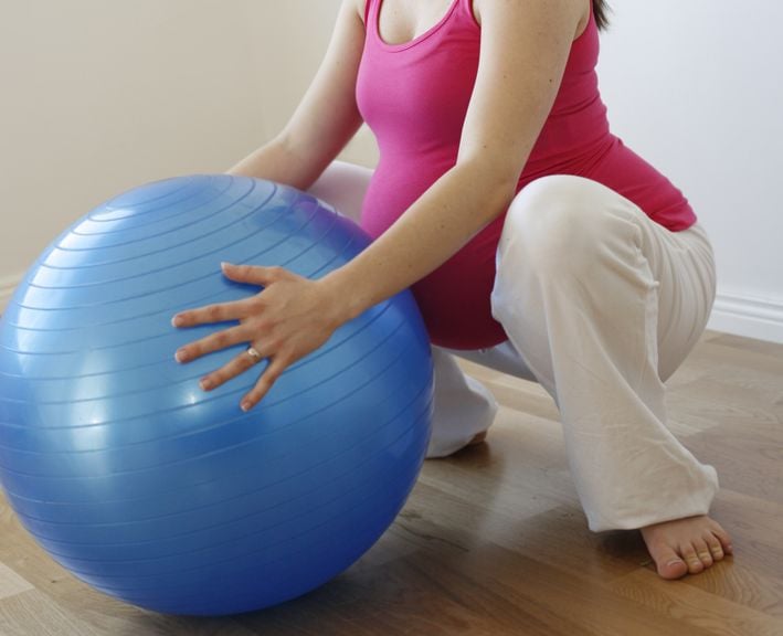 Schwangere in der Hocke mit Gymnastikball