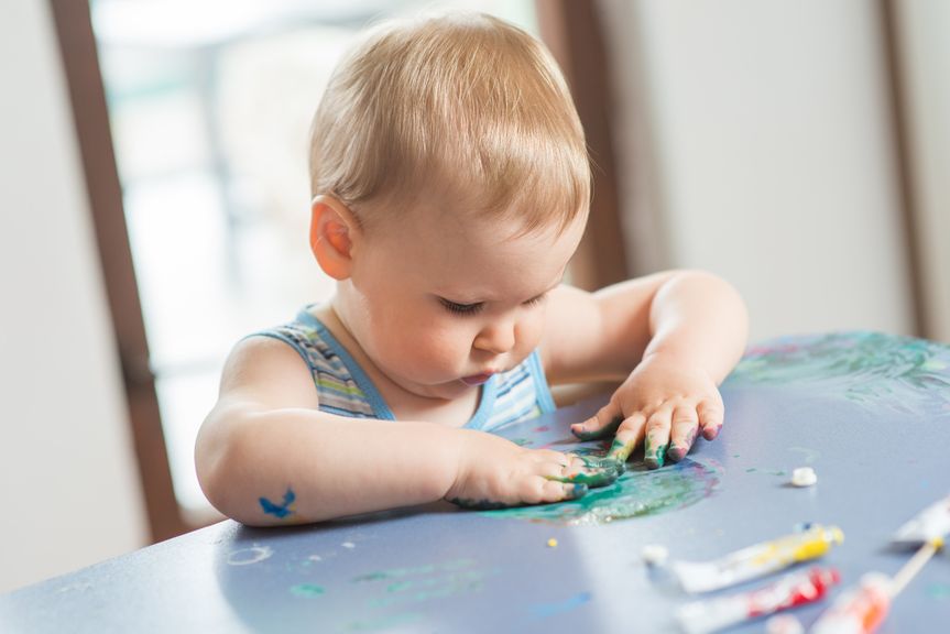 Baby matscht, schmiert mit Farben auf dem Tisch