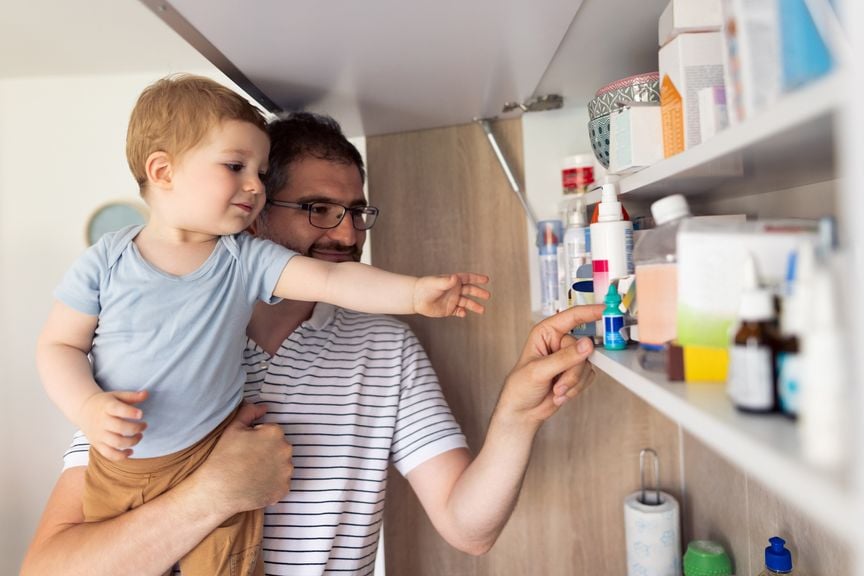 Vater hält  Sohn auf dem Arm und nimmt Medikament aus der Hausapotheke