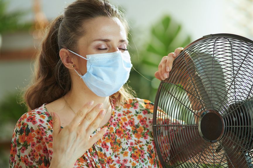 Frau mit Hygienemaske vor einem Ventilator