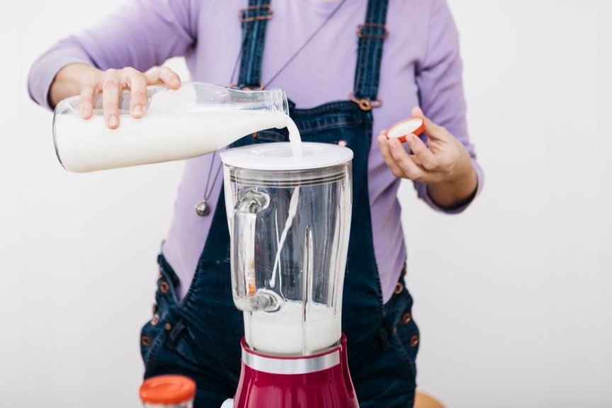 Schwangere giesst Milch in den Mixer für Smoothie