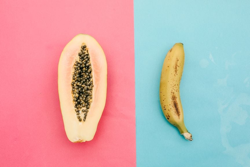 Eine halbierte Papaya und eine Banane mit Schale vor rosarotem und hellblauem Hintergrund
