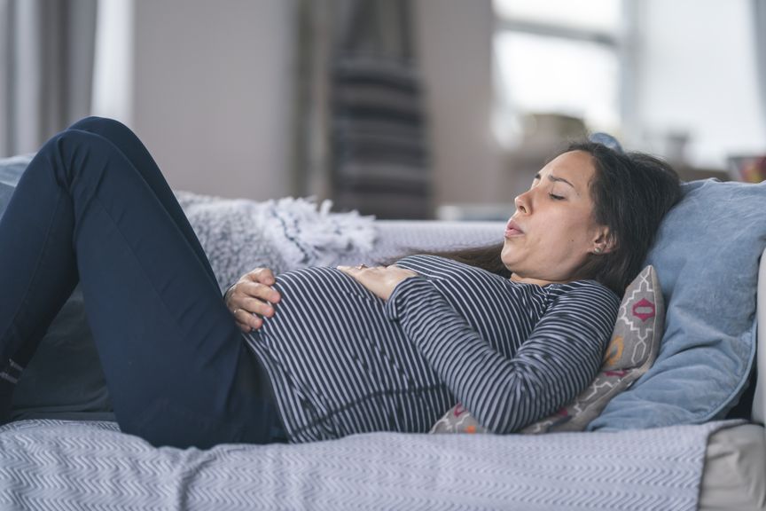 Schwangere liegt auf dem Sofa und atmet schwer