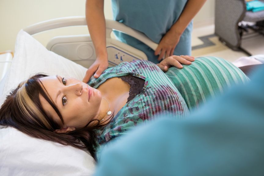 Schwangere im Spitalbett, wird von Hebamme betreut 