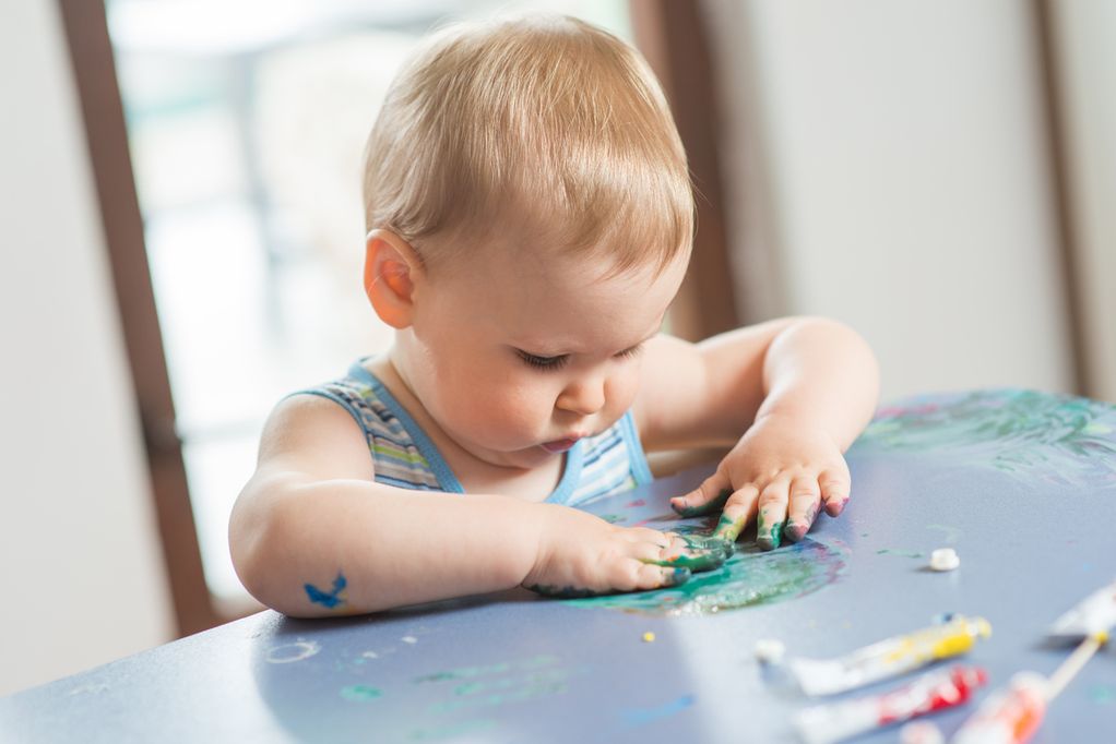 Baby matscht, schmiert mit Farben auf dem Tisch