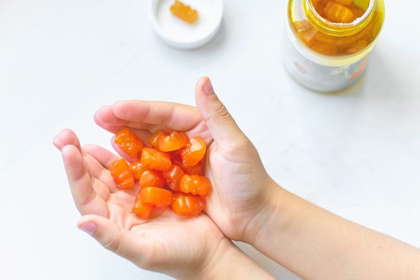 Kinderhände mit orangefarbenen Vitamingummibärchen