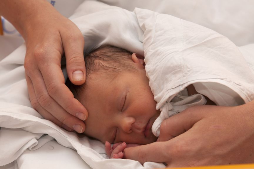 schlafendes Neugeborenes wird am Kopf und Händen berührt