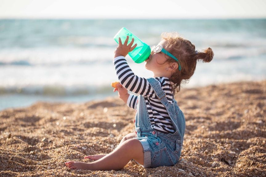 Kind trinkt im Sand sitzend