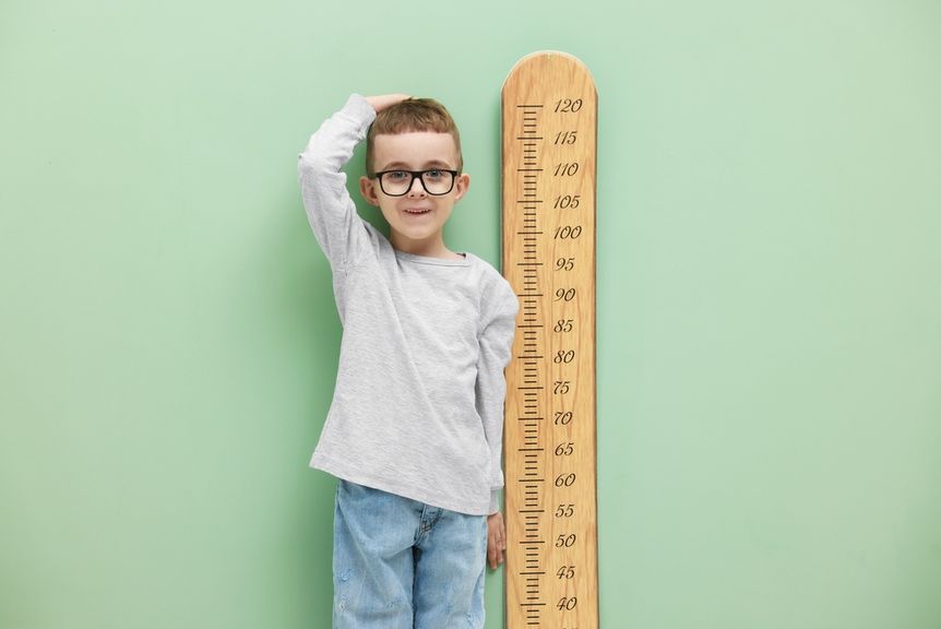 Kind mit Brille steht neben einer Messlatte