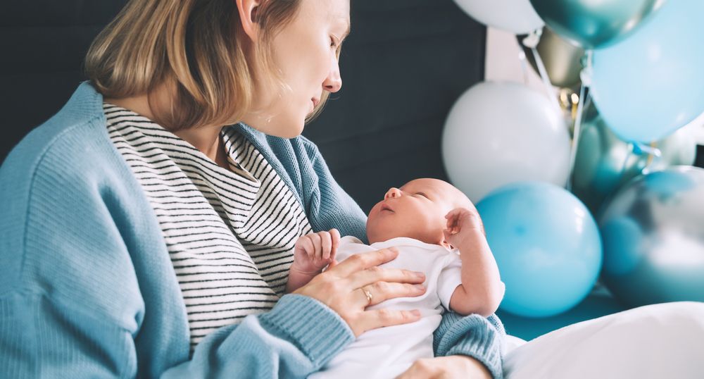 Mutter mit Baby im Arm und Luftballons im Hintergrund