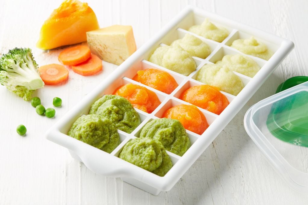 Gemüsestücke und püriertes Gemüse in Eiswürfelbehälter zum Einfrieren