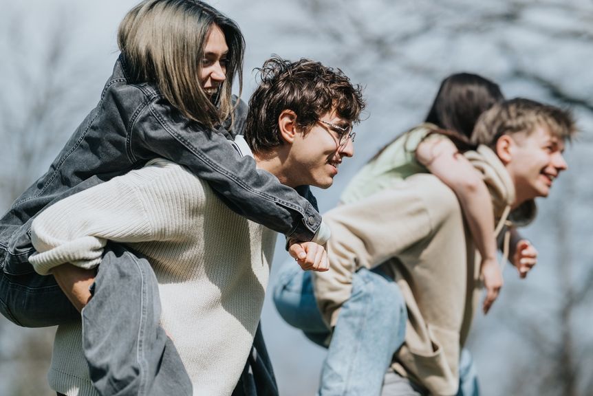 Lachende junge Männer tragen fröhliche junge Frauen auf ihrem Rücken
