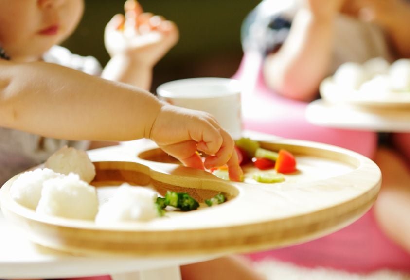 Kleinkind isst im Hochstuhl Fingerfood mit Händen