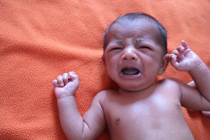 Weinendes Neugeborenes liegt auf einer orangefarbenen Decke