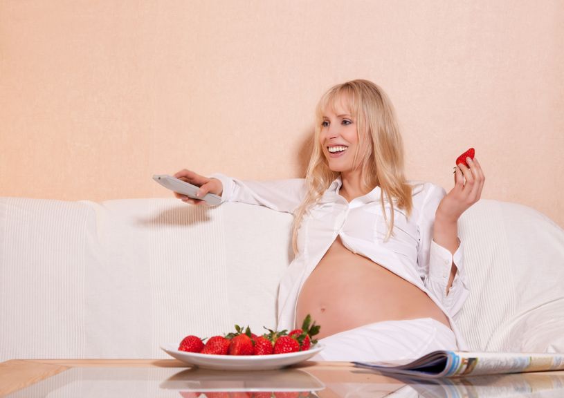 Schwangere Frau beim Fernsehen mit Erdbeere in der Hand