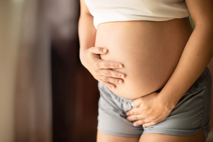 Schwangere hat die Hände am Bauch und dem Schambereich