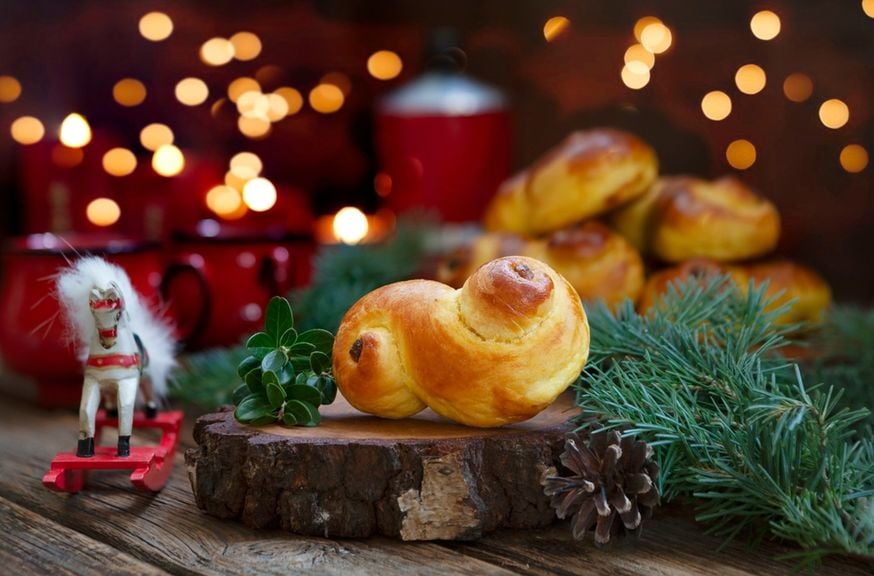 Schwedische Lussebullar mit Tannenzweigen, Spielzeug-Schaukelpferd und Weihnachtslichtern