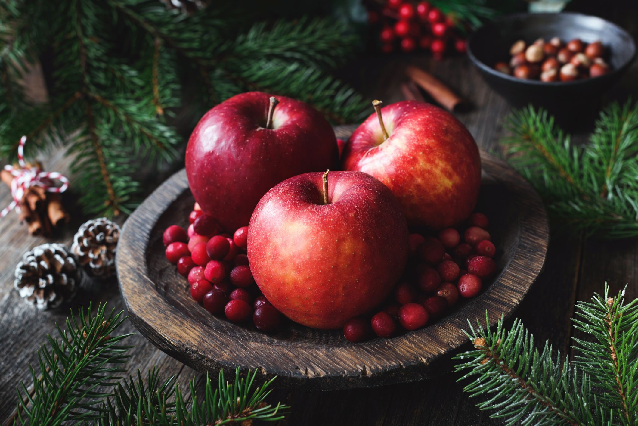Rote Äpfel und Cranberries auf einem Teller, umgeben von weihnachtlicher Dekoration