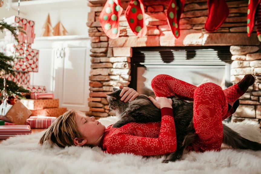 Kind liegt mit einer Katze im weihnachtlich geschmückten Wohnzimmer auf dem Teppich