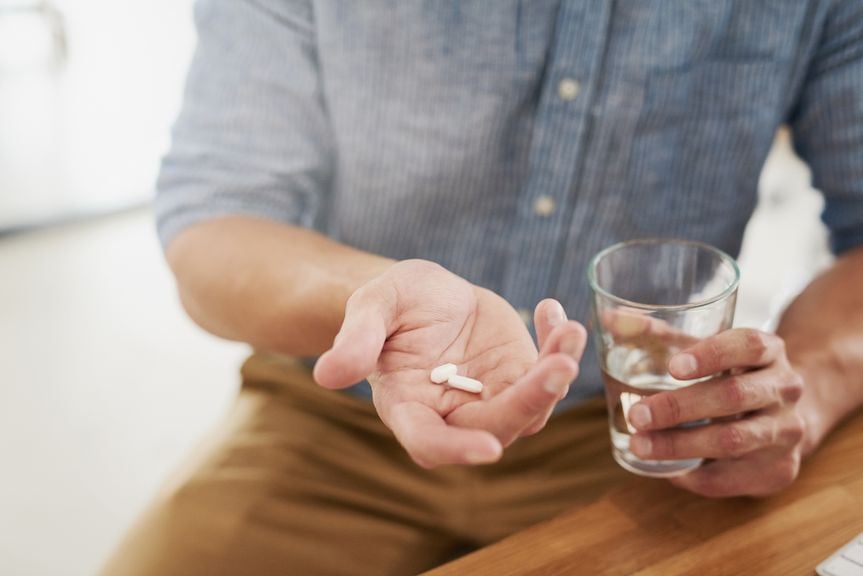 Mann mit Medikamenten und Wasserglas in der Hand