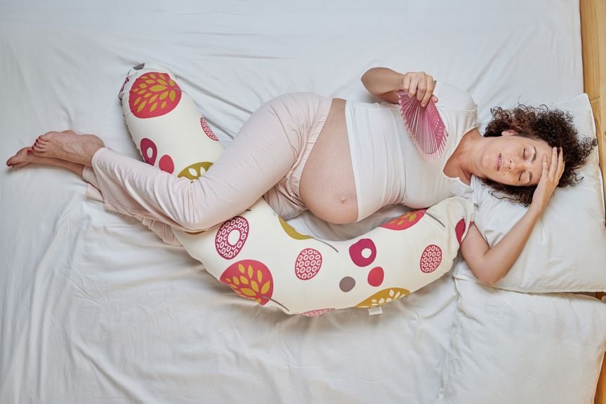 Schwangere Frau hält einen Fächer in der Hand und versucht, bei Hitze zu schlafen
