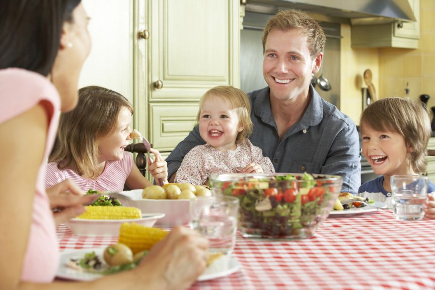 Familie sitzt am Esstisch bei einer Mahlzeit mit Salat und Gemüse